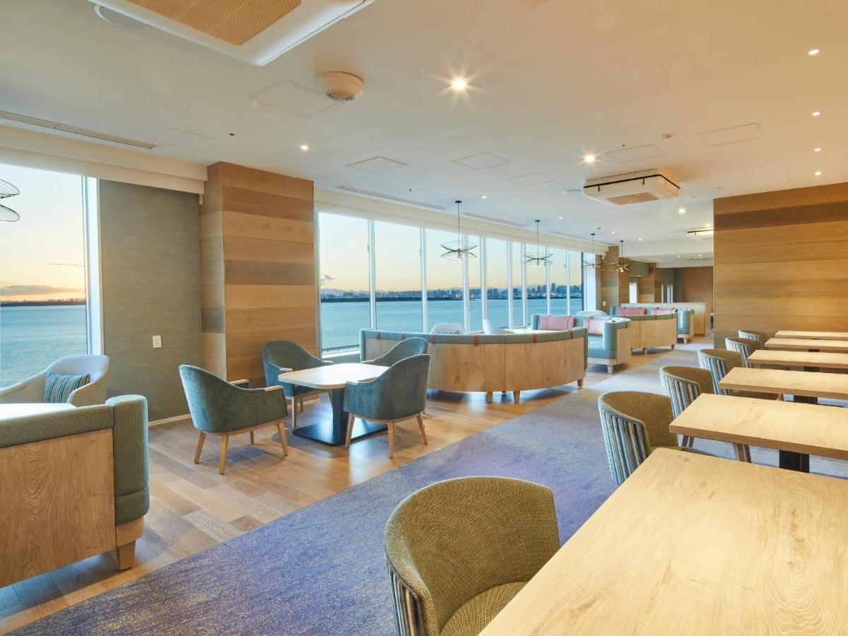 Готель Grand Nikko Tokyo Bay Maihama Urayasu Екстер'єр фото The photo shows a modern interior space, likely a dining or lounge area. It features large windows that offer a view of the water, allowing natural light to fill the room. The decor includes wooden walls and stylish, comfortable furniture, with sever