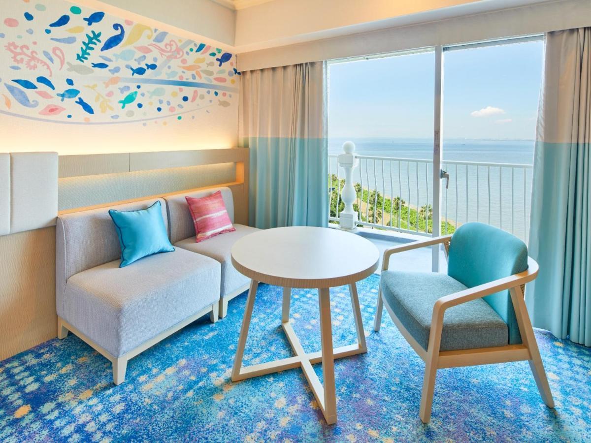 Готель Grand Nikko Tokyo Bay Maihama Urayasu Екстер'єр фото The photo shows a modern and stylish interior of a room with a view. There is a cozy seating area featuring a light-colored sofa with decorative cushions in various shades of blue and pink. A round table occupies the center of the space, surrounded b
