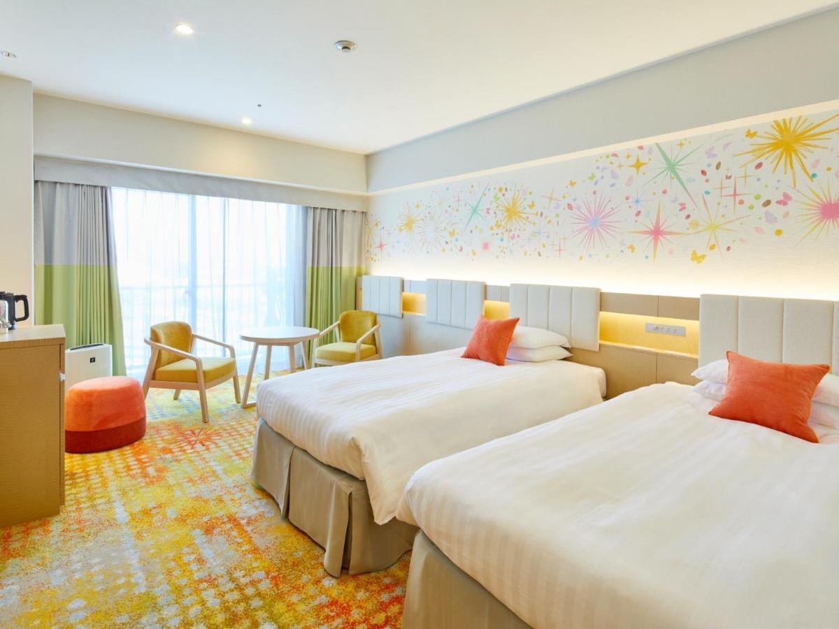 Готель Grand Nikko Tokyo Bay Maihama Urayasu Екстер'єр фото The photo shows a modern hotel room featuring two twin beds with light-colored bedding and decorative orange cushions. There is a vibrant, colorful carpet on the floor, and the walls are adorned with playful designs, including bursts of color. A larg