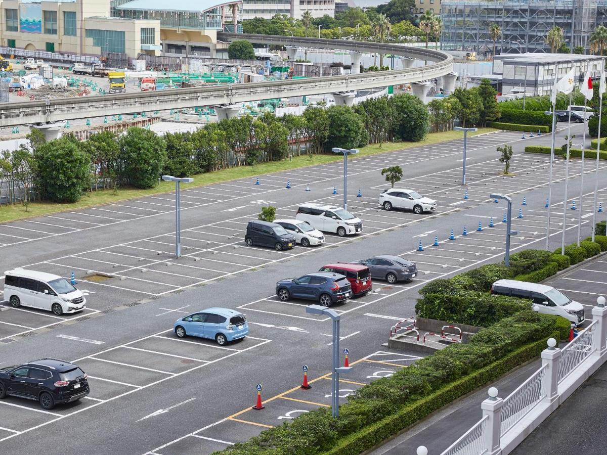 Готель Grand Nikko Tokyo Bay Maihama Urayasu Екстер'єр фото The photo shows a partially empty parking lot with several parked cars. In the foreground, there are a few vehicles, including a blue car and a white one. The lot has clearly marked parking spaces, and there are some trees and shrubs along the sides.