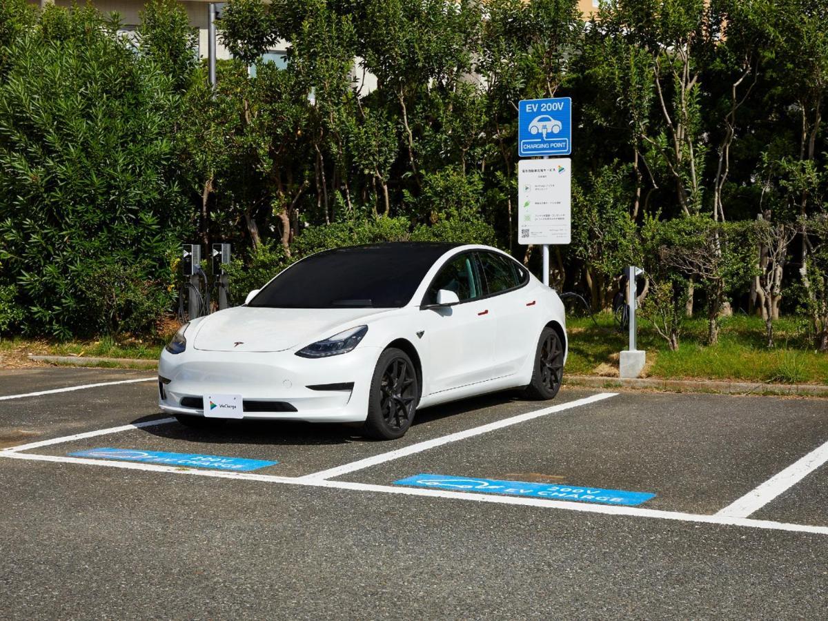 Готель Grand Nikko Tokyo Bay Maihama Urayasu Екстер'єр фото The photo shows a white electric car parked in an EV (electric vehicle) charging spot. The car has a sleek design with black wheels and tinted windows. In the background, there are green shrubs and trees, indicating a natural or landscaped environmen