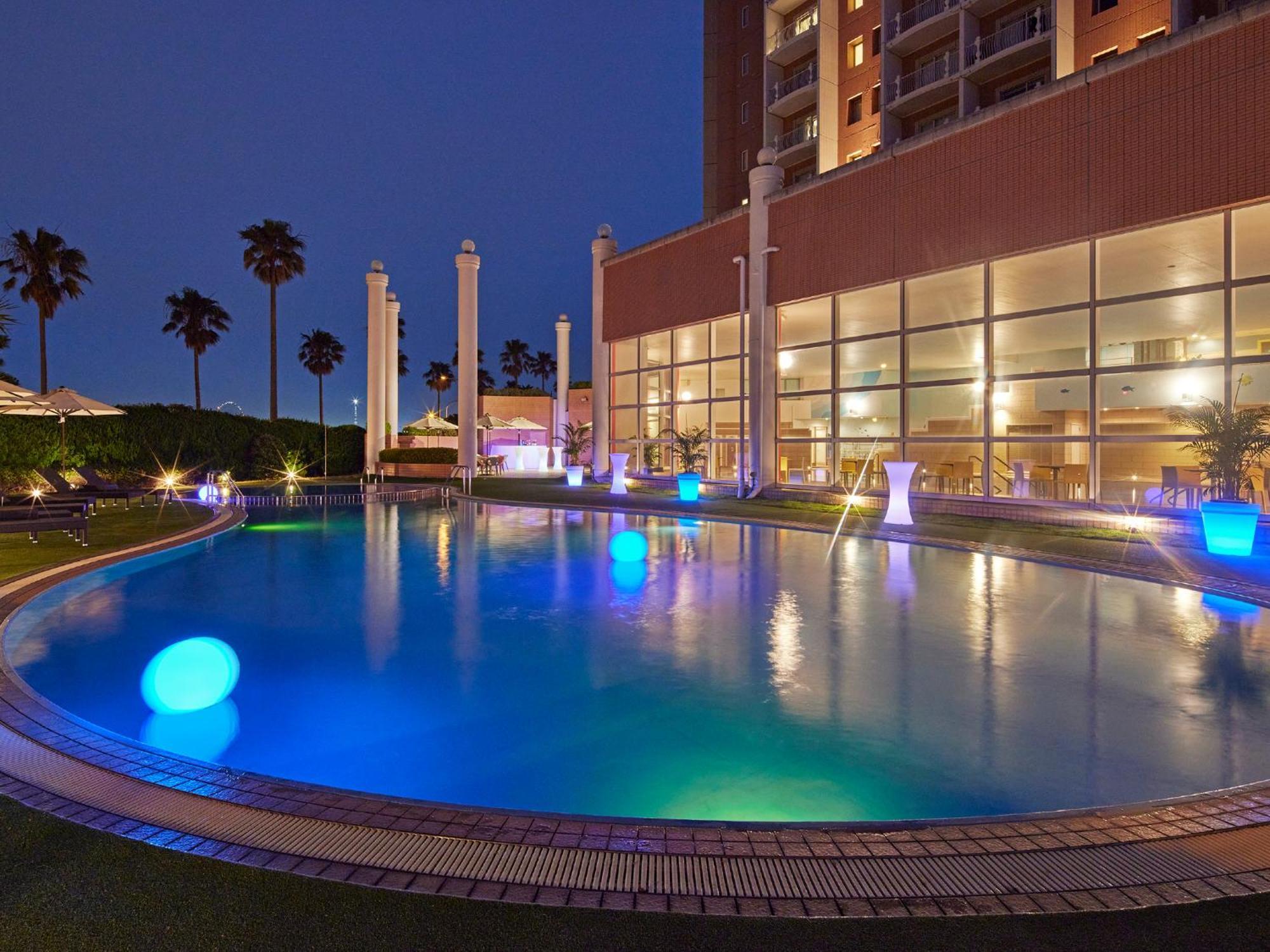 Готель Grand Nikko Tokyo Bay Maihama Urayasu Екстер'єр фото The photo shows a well-lit swimming pool at night, surrounded by a lush green area. The pool features glowing blue lights that create a serene and inviting atmosphere. Palm trees can be seen in the background, adding a tropical feel to the scene. Add