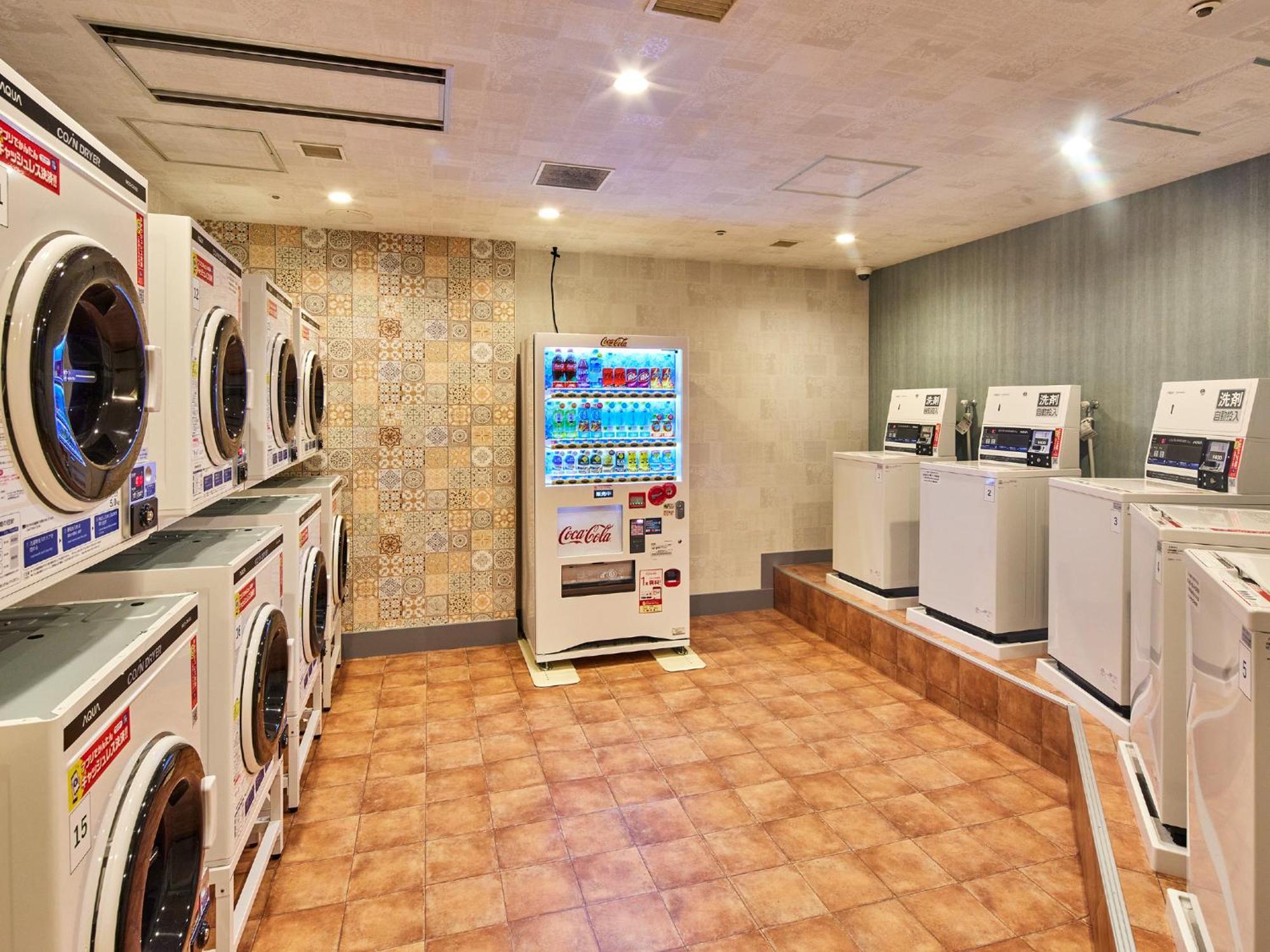 Готель Grand Nikko Tokyo Bay Maihama Urayasu Екстер'єр фото The photo shows a laundry room equipped with several washing machines and dryers. On the left side, there are multiple front-loading washing machines arranged in a row, and on the right side, there are dryers. In the center, there is a vending machin