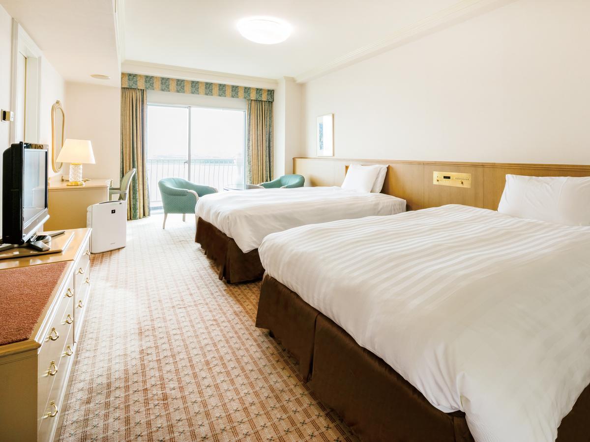 Готель Grand Nikko Tokyo Bay Maihama Urayasu Екстер'єр фото The photo shows a hotel room featuring two large beds with white bedding and brown bases. There's a light-colored carpet on the floor, and the room is brightly lit. To one side, there is a television on a stand and a small white refrigerator. A desk 